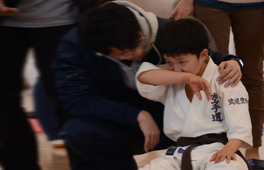 悔し涙をこらえる子供の肩に手を添える指導員